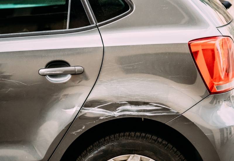 The rear driver's side wheel well of a gray SUV shows that there is a large scratch in the paint above the tire.